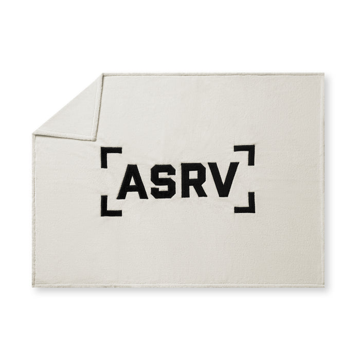 flatlay Sherpa Recovery Blanket in ivory cream with black ASRV logo, folded corner view