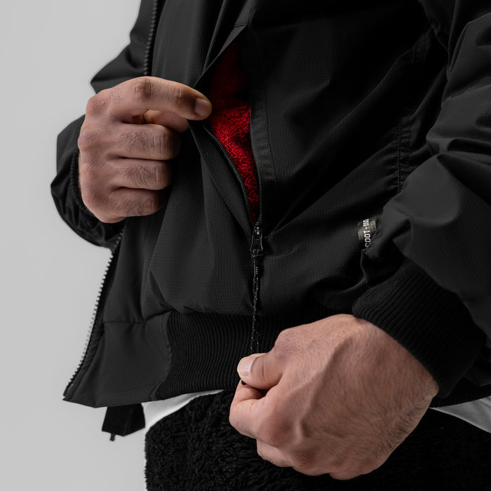 Sherpa-lined insulated bomber jacket in black, worn and zipped open to show red interior lining