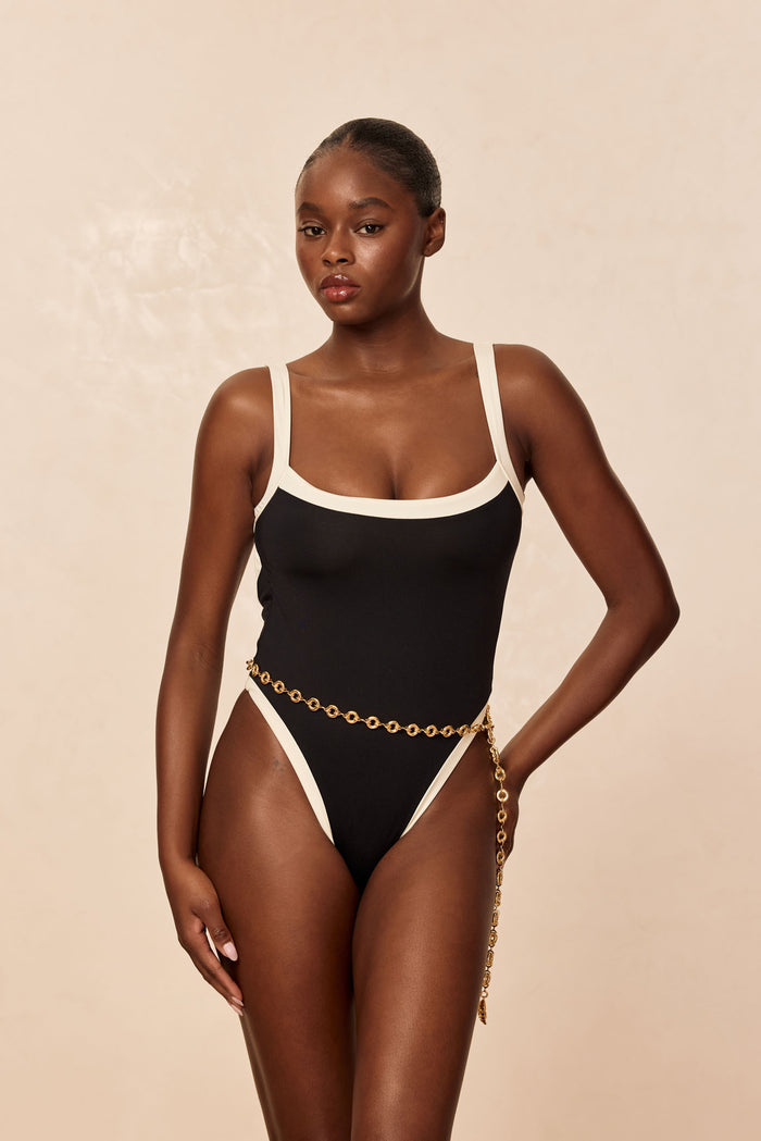 Front view of Barcelona One Piece Black/Ivory on model, fitted square neckline, ivory trim, high-cut leg, beige background