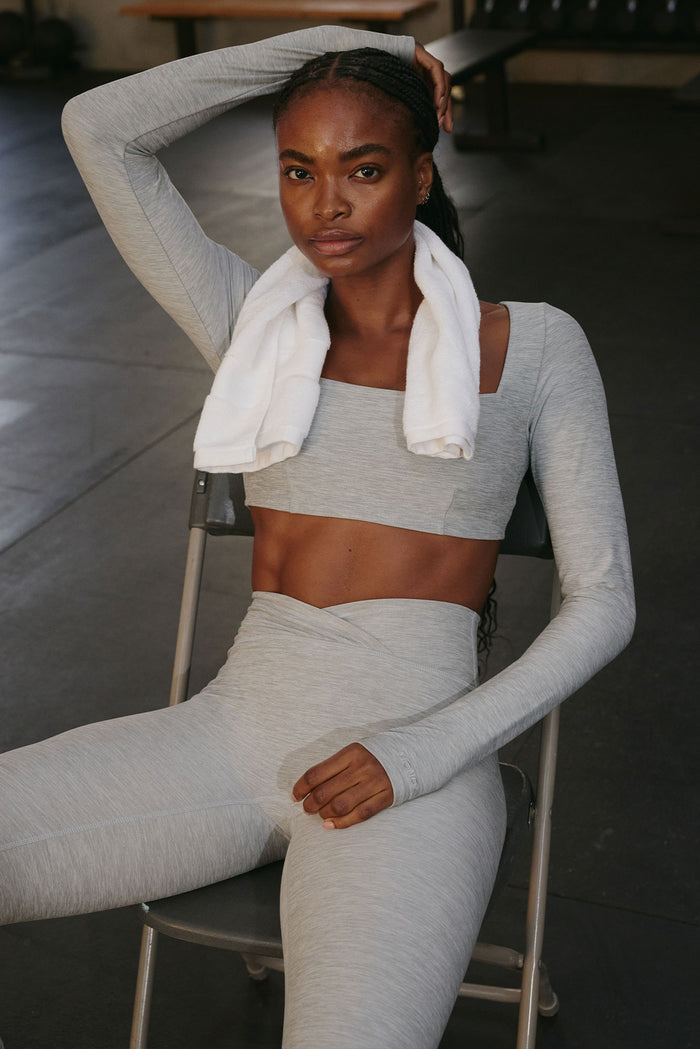 Seated front view of Bellevue Top in heather grey with square neckline, long sleeves with thumb holes, cropped fit