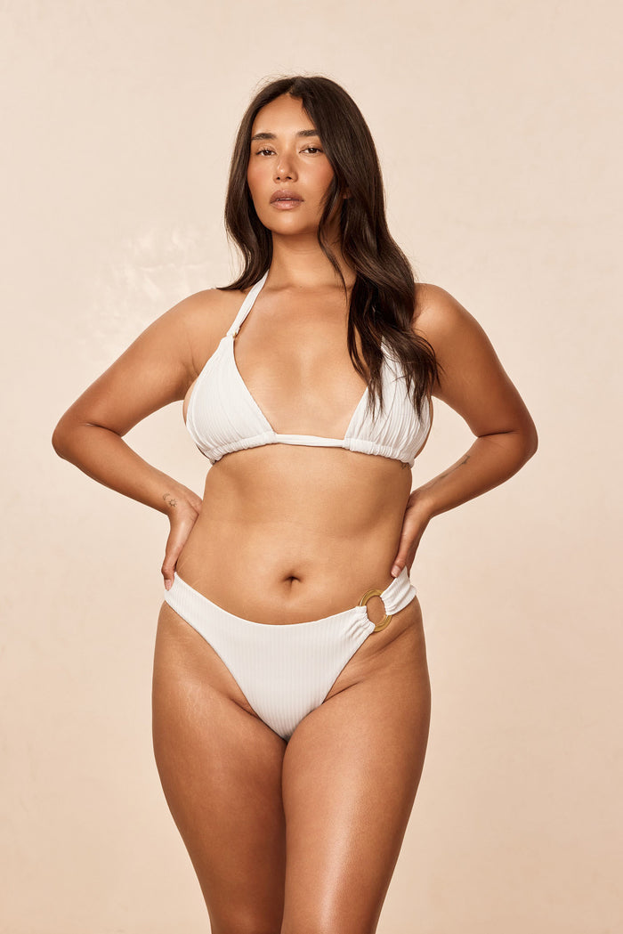 Front view of Bronte Bottom - White Rib on model, high-cut mid-rise cheeky style with gold ring detail on beige background