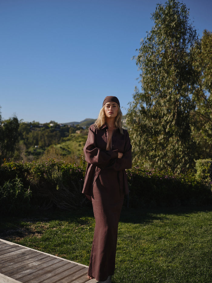Full-length front view of Fontelina linen skirt in espresso showing high waist and column silhouette on model with matching linen shirt in a sunny garden