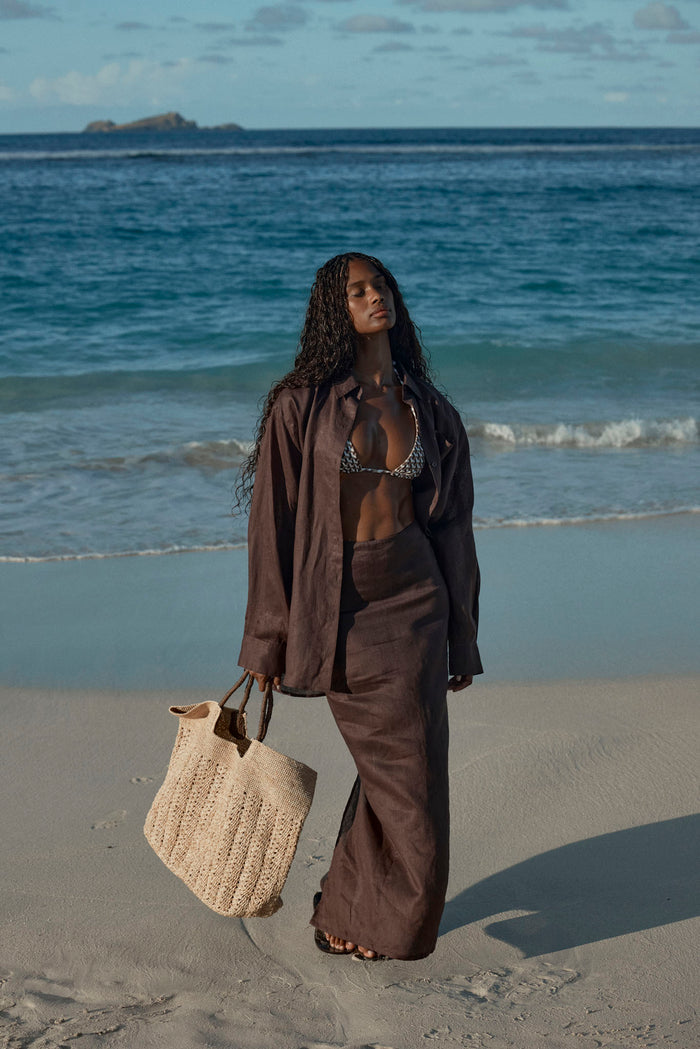 Front view of Fontelina Linen Skirt in espresso linen, high-waist skirt with front slit and matching linen shirt on a beach