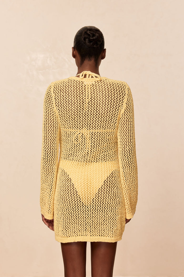 Back view of Montego Mini Dress in Honey petit crochet showing open-knit texture, sleeves and tie-back on beige