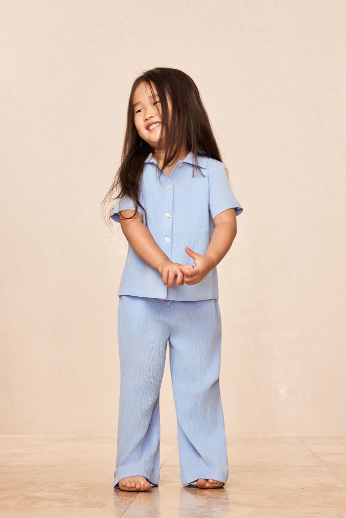 Front view of Pacific Beach Shirt Kids in Sky showing short-sleeve button-front crinkle fabric on child model, beige backdrop