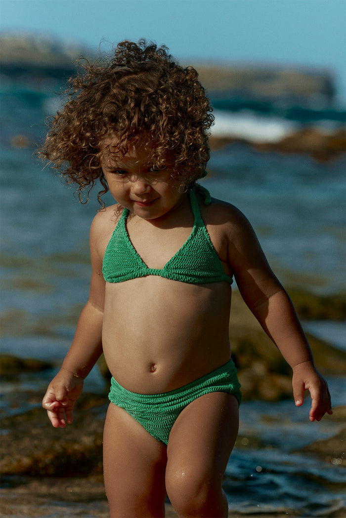 Front of Palma Top & Seychelles Bottom Set showing green textured halter and matching bottoms worn by a child at a rocky shore