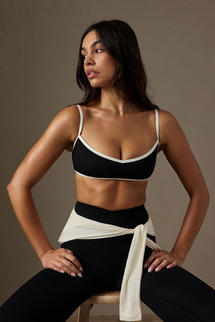 Three-quarter view of Soho Bra in black/ivory showing V-neck, adjustable straps, and contrast trim on neutral background