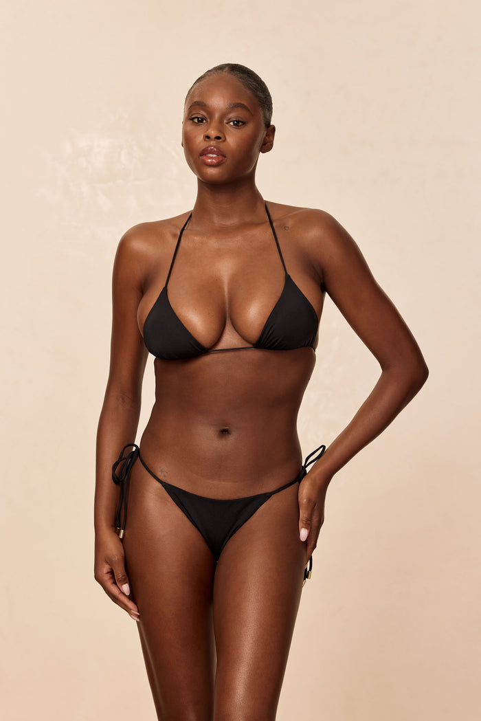 Front view of Taormina Top in black on model, triangle cups with thin halter and underbust tie, beige studio background