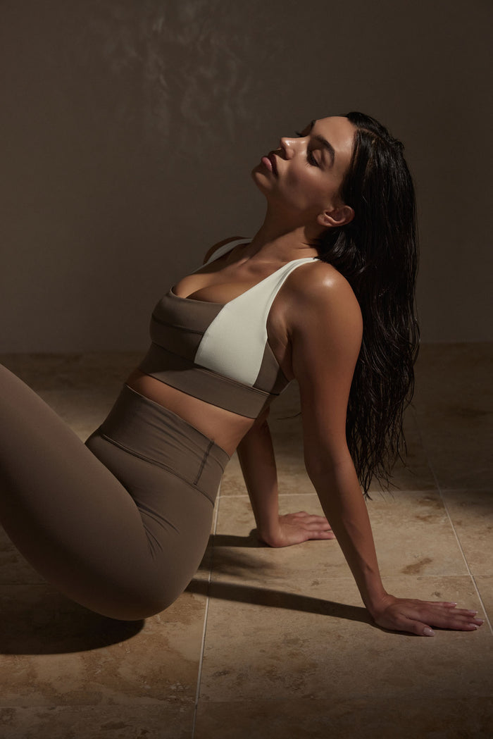 Three-quarter view of Tash Bra in stone and ivory showing colorblock scoop neckline and supportive band on seated model