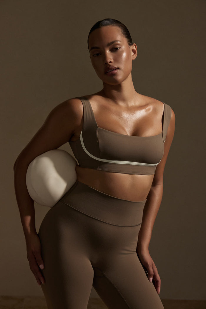 Three-quarter view of Zion Bra in Stone/Ivory Jersey on model showcasing square neckline, contour seaming, and ivory contrast piping against a neutral studio background